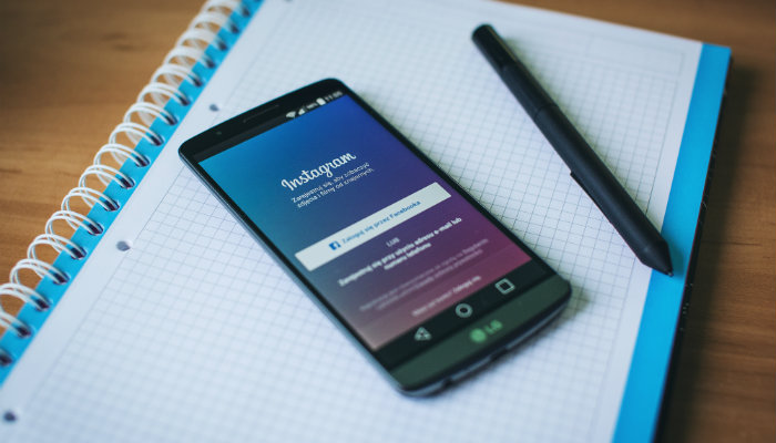 marketing no instagram celular e caneta preta em cima de uma caderno quadriculado