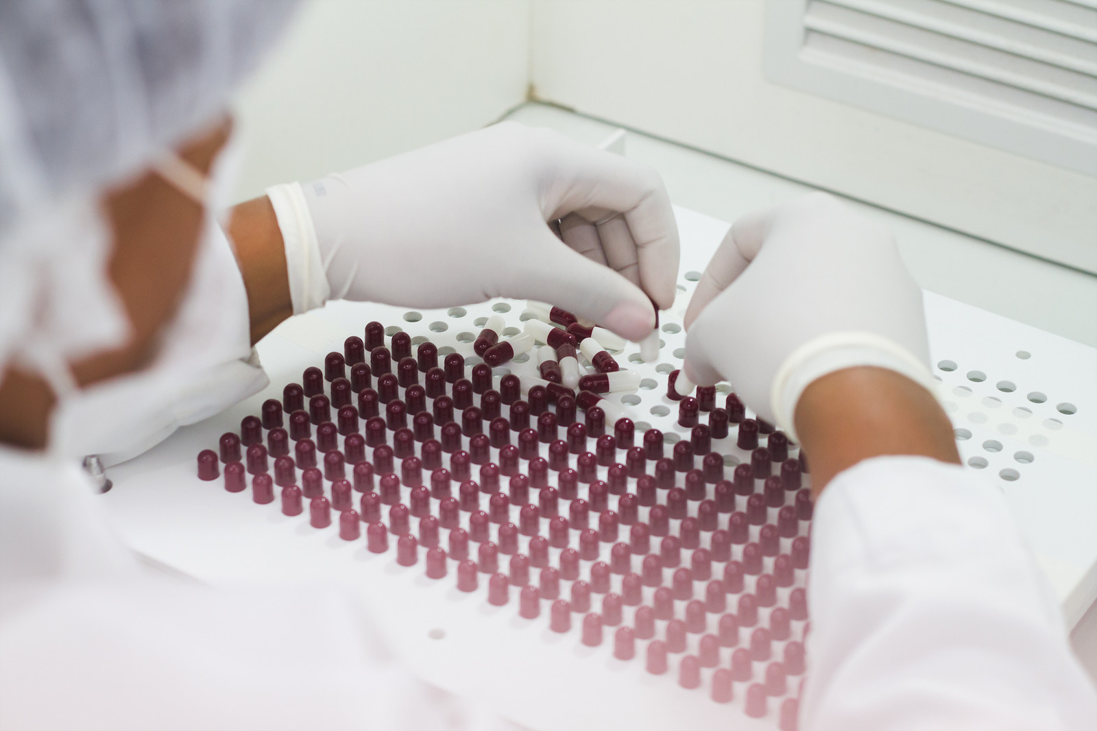 imagem de uma mão manuseando cápsulas em um tabuleiro de laboratório
