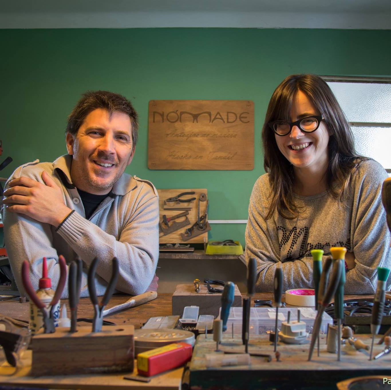 Nicolas y Belen en el taller de anteojos de madera, frente a la cámara desde la mesa de trabajo 