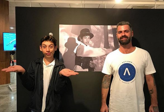 Autista contempla exposição da suas fotos com o fotografo Leonardo, vestindo camiseta da Rockfella em parceria com a ong autonomia