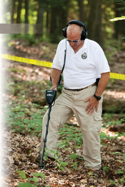 Foto policial com um detector de metal CSI PRO Garrett procurando objetos de cenas do crime