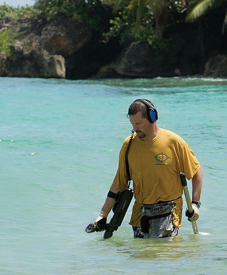 Figura detector ATX com uma pessoa procurando na praia de água salgada com o detector todo dentro da água
